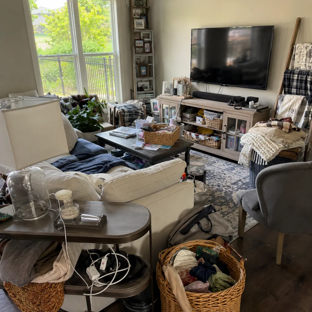 Realistic editorial photo of a living room with crowded surfaces, extra chairs, baskets, blankets, cords, and storage furniture showing no place for returns and