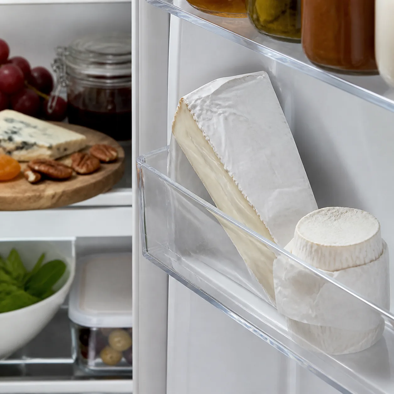 Realistic editorial photo of brie and goat cheese packages tucked into a refrigerator door shelf, cheese board items nea