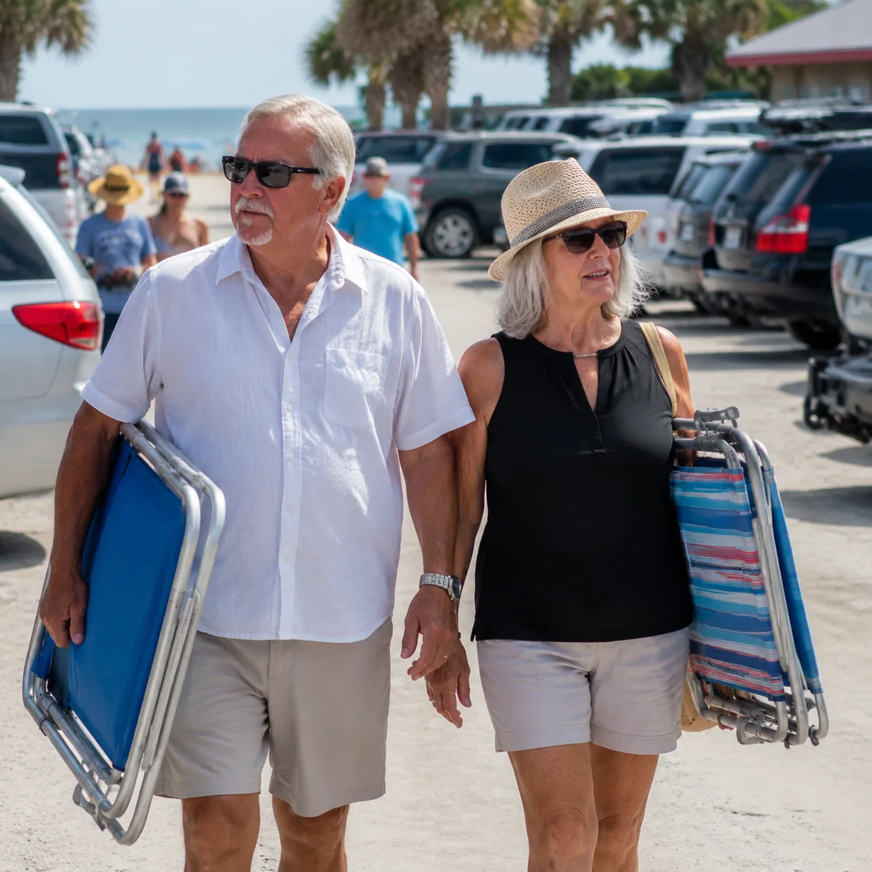 older couple carrying beach chairs through crowded Florida beach parking area, realistic editorial lifestyle photography
