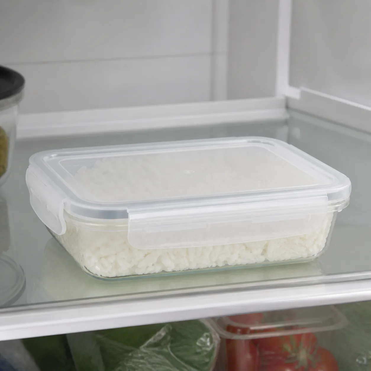 Realistic editorial photo of a container of cooked rice cooling in a shallow sealed container on a refrigerator shelf, s