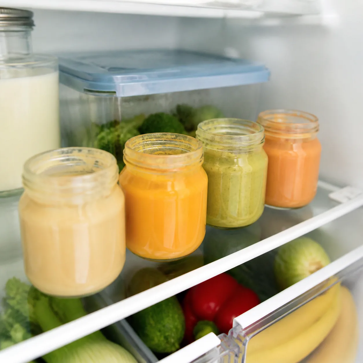 Realistic editorial photo of opened jars of baby food placed on an interior refrigerator shelf, clean family kitchen, so