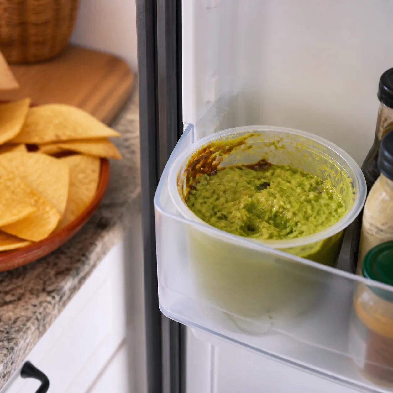 Realistic editorial photo of an opened container of guacamole browning at the edge in a refrigerator door compartment, t