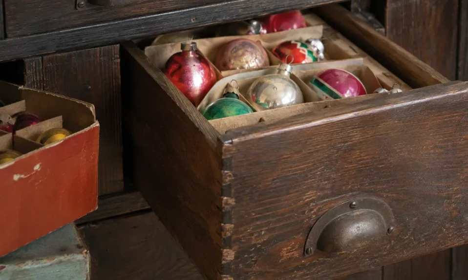Realistic editorial photo of close-up antique furniture details with drawers, joints, hardware, and old wood grain showing old christmas ornaments in boxes