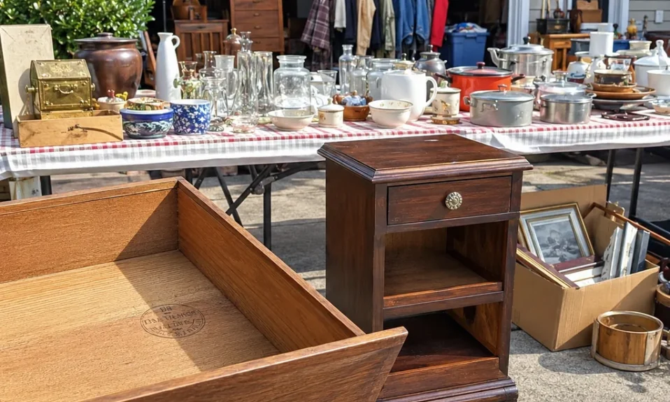 Realistic editorial photo of an American garage sale with folding tables, boxes, old kitchen items, furniture, and collectibles showing maker's marks under draw